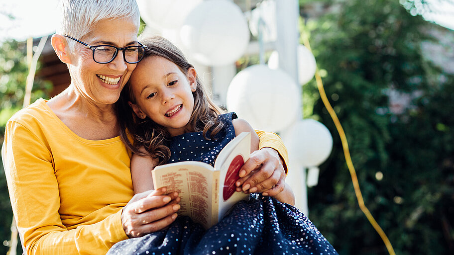 Ältere Frau liest Mädchen aus Buch vor