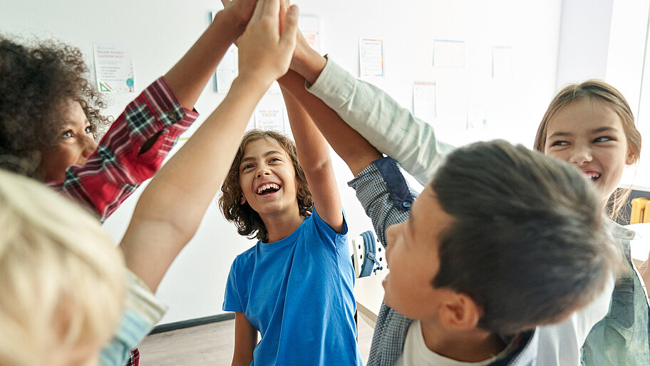 Glückliche Gruppe von Schülerinnen und Schüler geben sich zuammen im Klassenzimmer High Five