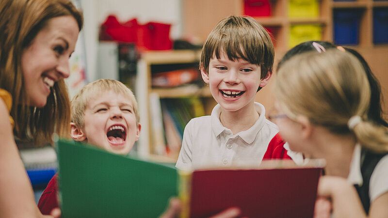 Lehrerin sitzt mit ihren Grundschülern im Klassenzimmer und zeigt ihnen ein Buch