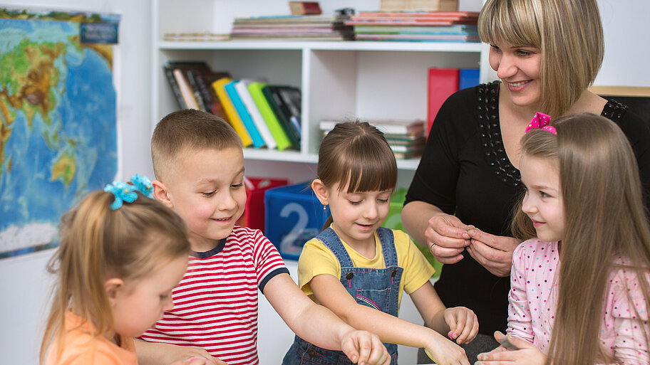 Jüngere Schülerinnen und Schüler mit Lehrerin beim Kneten in Teamarbeit