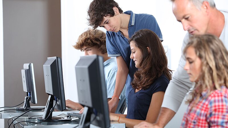 Schülerinnen und Schüler mit Lehrer vor Computern