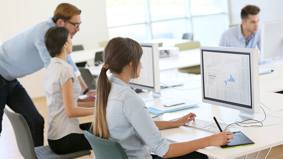 Personen, die im Büro vor PC und Bildschirm sitzen