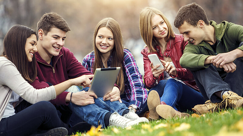 Gruppe von Teenager sitzen mit Laptop und Smartphone in der Wieseet and smart phone