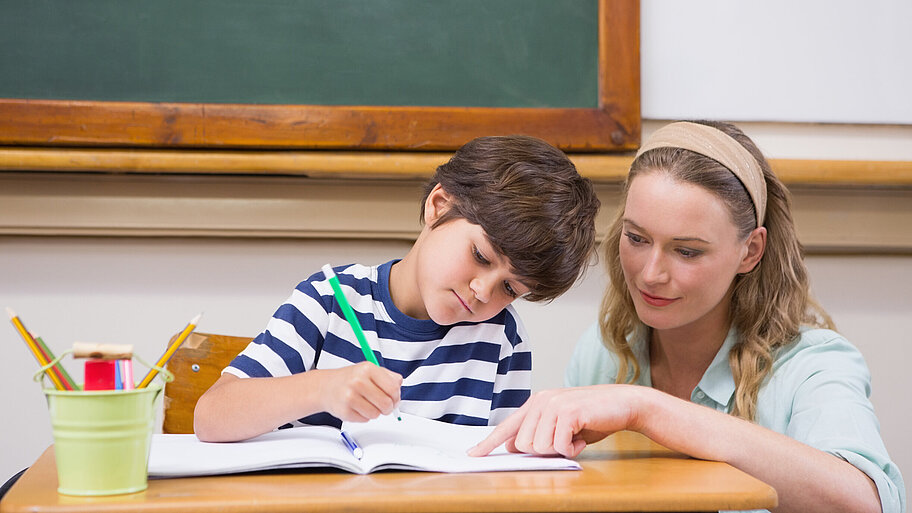 Lehrerin erklärt jungem Schüler eine Aufgabe, die dieser gerade bearbeitet