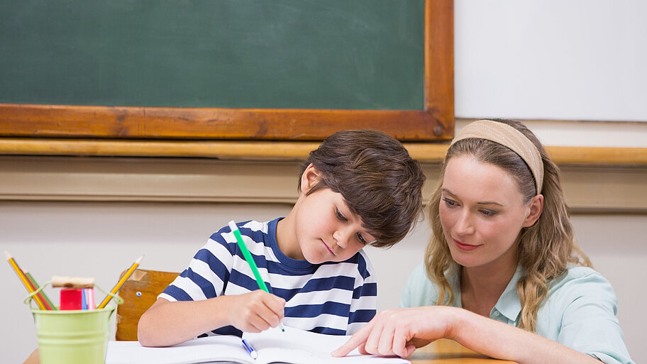 Lehrerin erklärt jungem Schüler eine Aufgabe, die dieser gerade bearbeitet