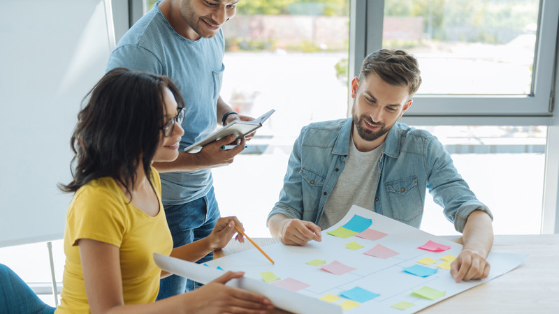 Drei Erwachsene betrachten ein Plakat und reden miteinander