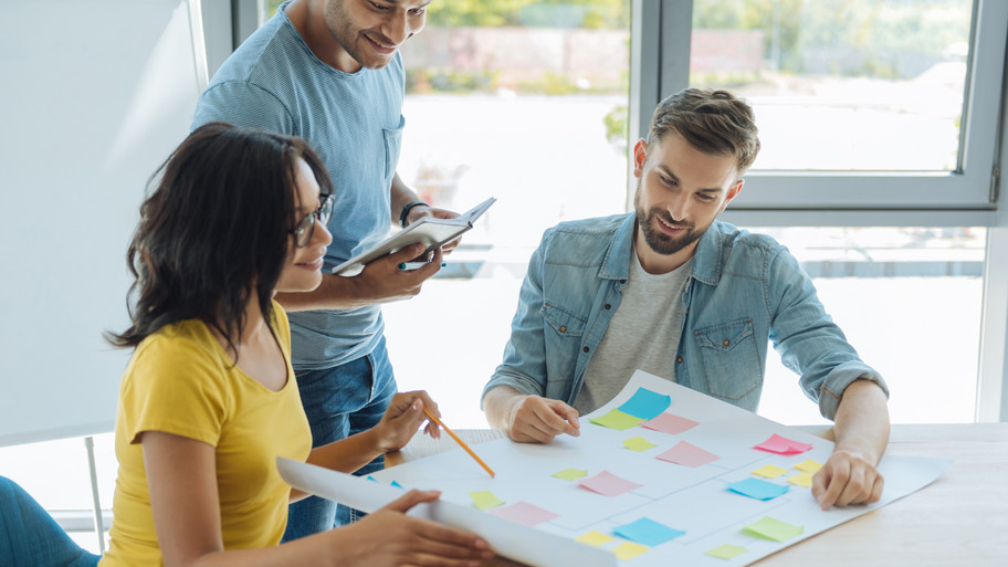 Drei Erwachsene betrachten ein Plakat und reden miteinander