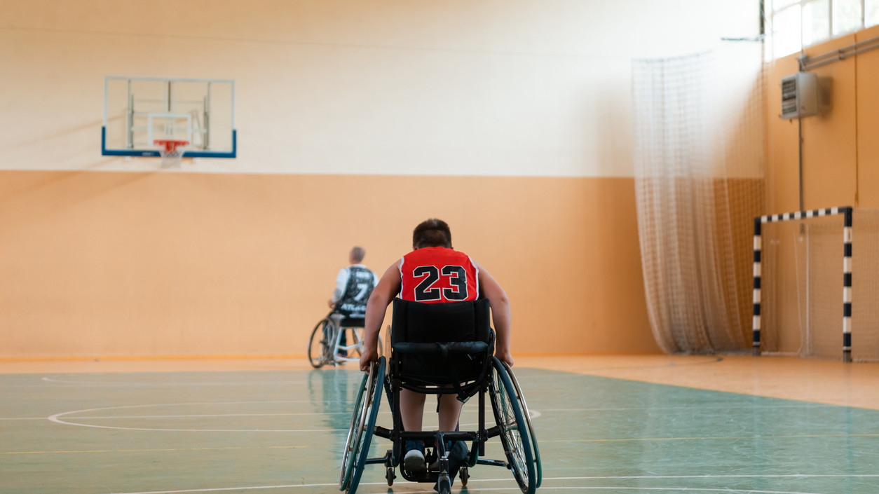Junge sitzt im Rollstuhl in einer Sporthalle