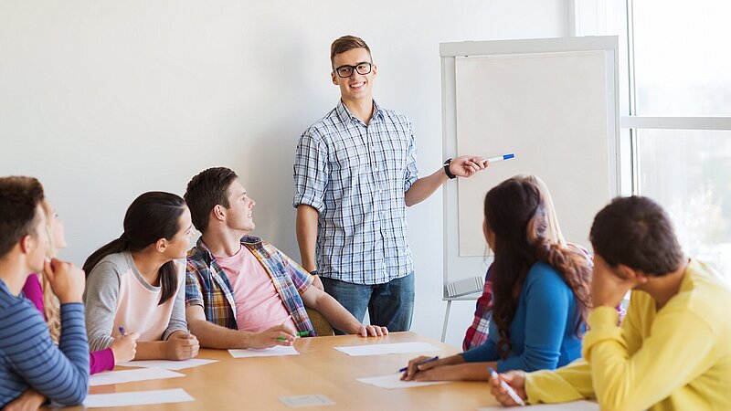 Lächelnde Schülerinnen und Schüler an einem Konferenztisch mit Whiteboard