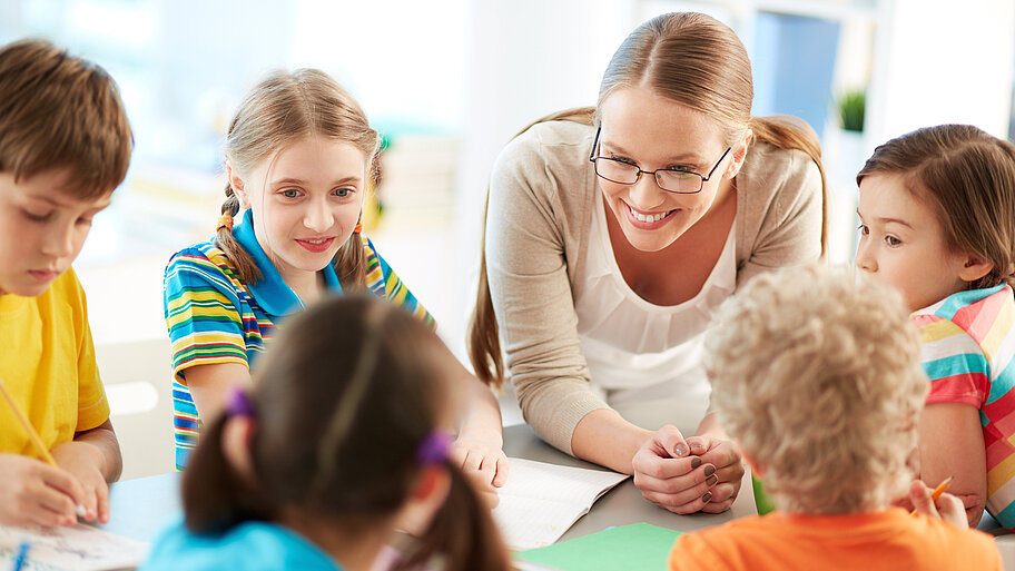 Lehrerin mit Schülern bei Gruppenarbeit im Gespräch