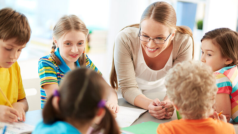 Lehrerin mit Schülern bei Gruppenarbeit im Gespräch