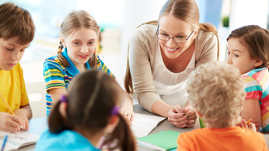 Lehrerin mit Schülern bei Gruppenarbeit im Gespräch