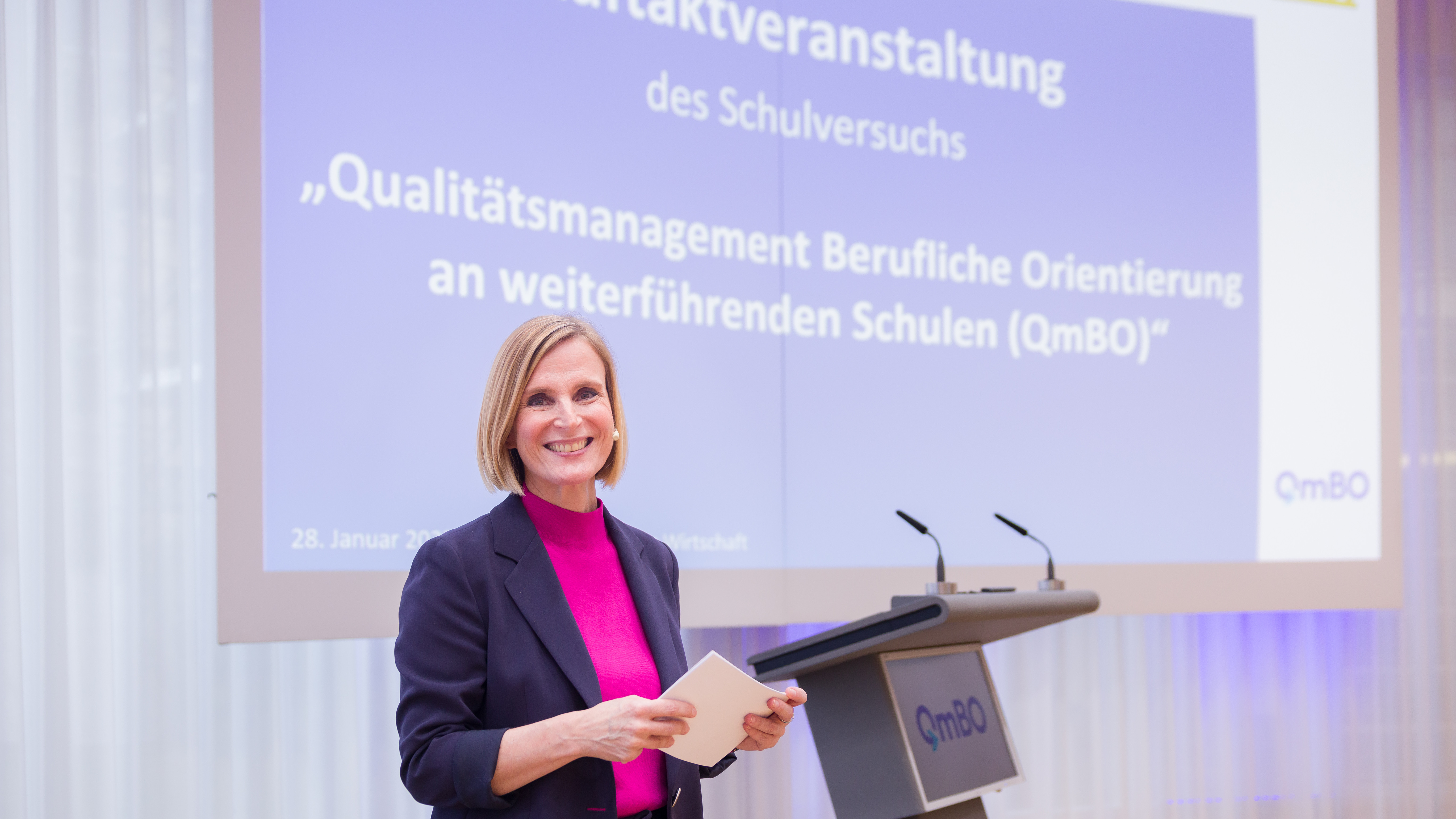Eine Frau moderiert vor eienr Leinwand eine Veranstaltung.