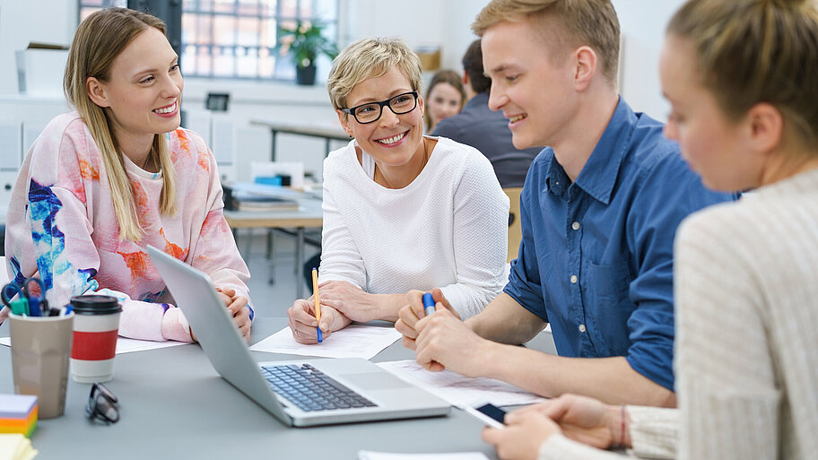Junge Erwachsene mit Lehrerin im Klassenzimmer bei einer Gruppenarbeit