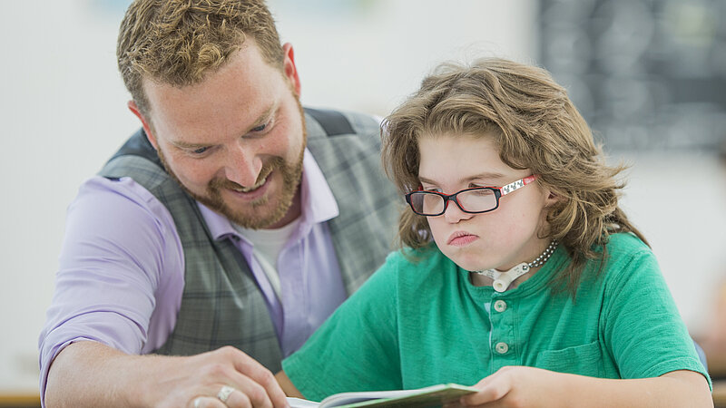 Lehrer unterstützt Schüler mit Behinderung beim Lesen. 