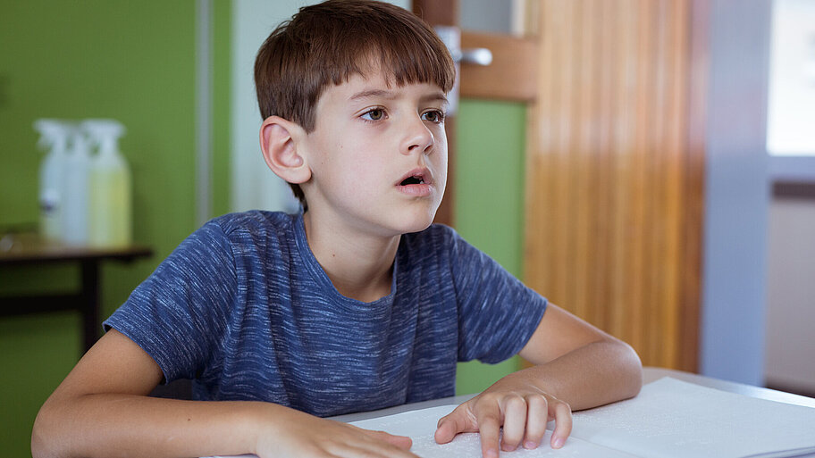 Blinder Schuljunge liest im Klassenzimmer mit den Fingern im Braille-Buch