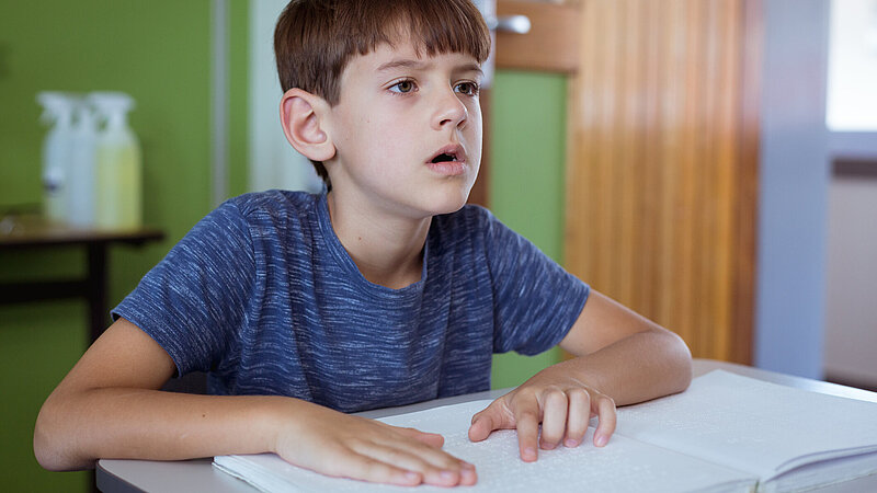 Blinder Schuljunge liest im Klassenzimmer mit den Fingern im Braille-Buch