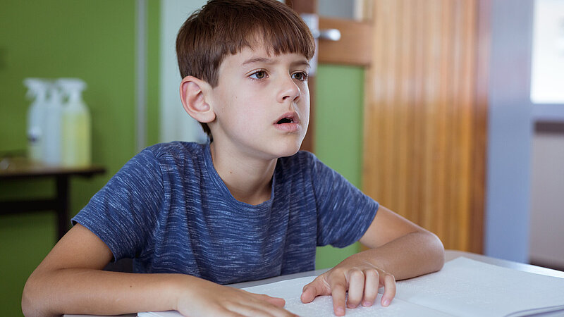 Blinder Schuljunge liest im Klassenzimmer mit den Fingern im Braille-Buch