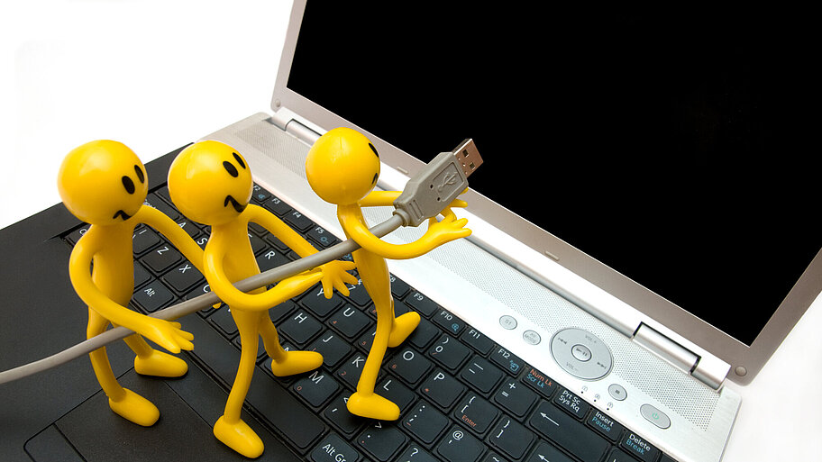 Symbolbild: Drei gelbe Smiley-Figuren stecken ein USB-Kabel in einen Laptop