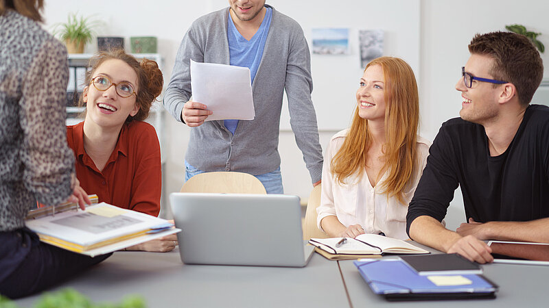 Gruppe junger Erwachsener mit Geschäftsunterlagen und Laptop bei einer Besprechung am Bürotisch