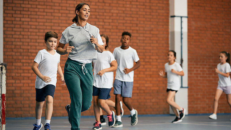 Sportlehrerin mit Schülern beim Laufen in der Turnhalle