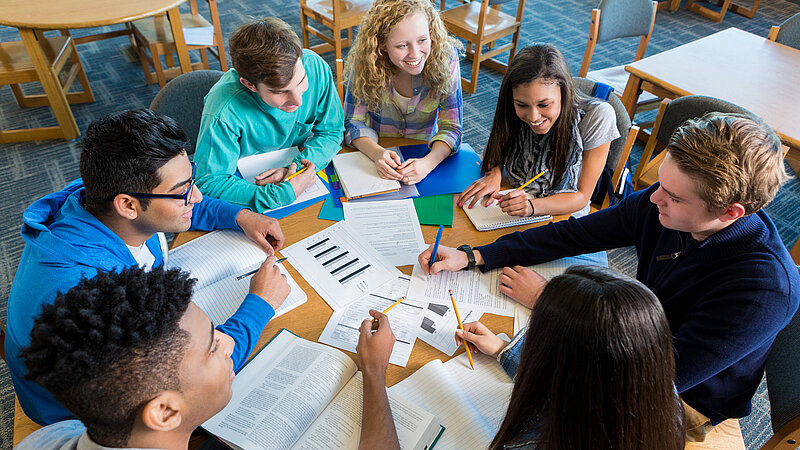 Schülerinnen und Schüler an rundem Tisch bei Gruppenarbeit. 