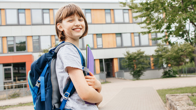 Junge Schülerin mit Rucksack und Unterrichtsmaterial auf einem Schulhof