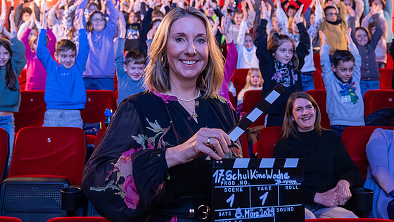 Frau Ministerin Stolz mit Filmklappe vor Kinopublikum