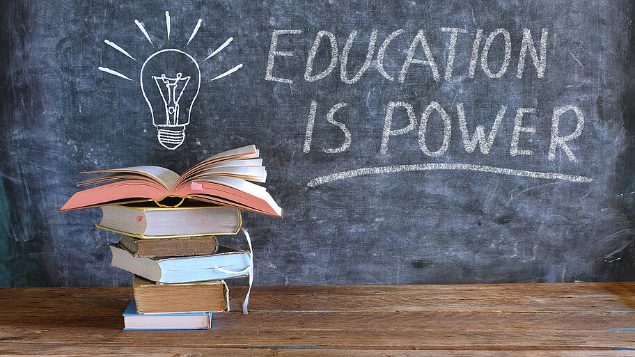 Bücherstapel mit Ideen-Glühbirme und Tafel-Schriftzug "Education is power"