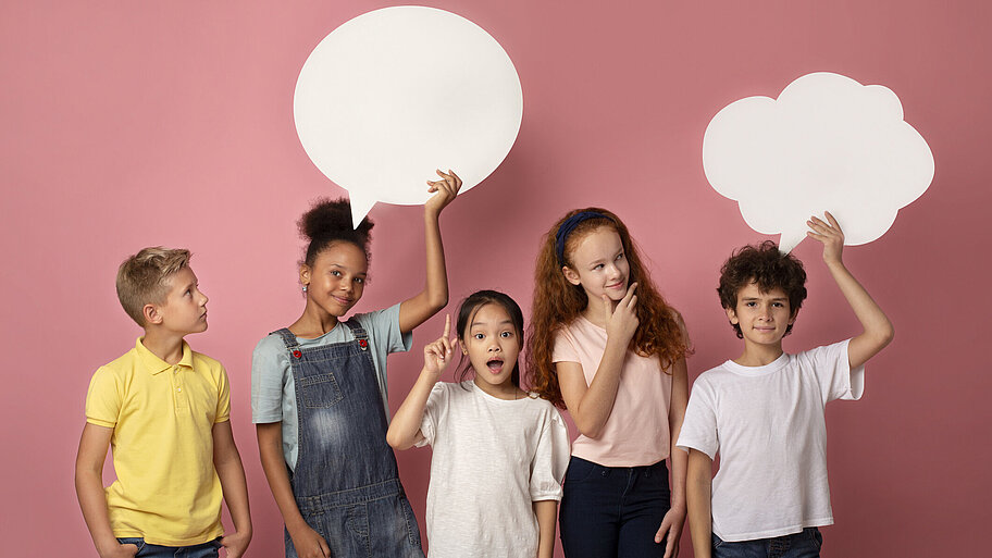 Fröhliche multinationale Schulkinder mit leeren Sprechblasen über rosa Hintergrund
