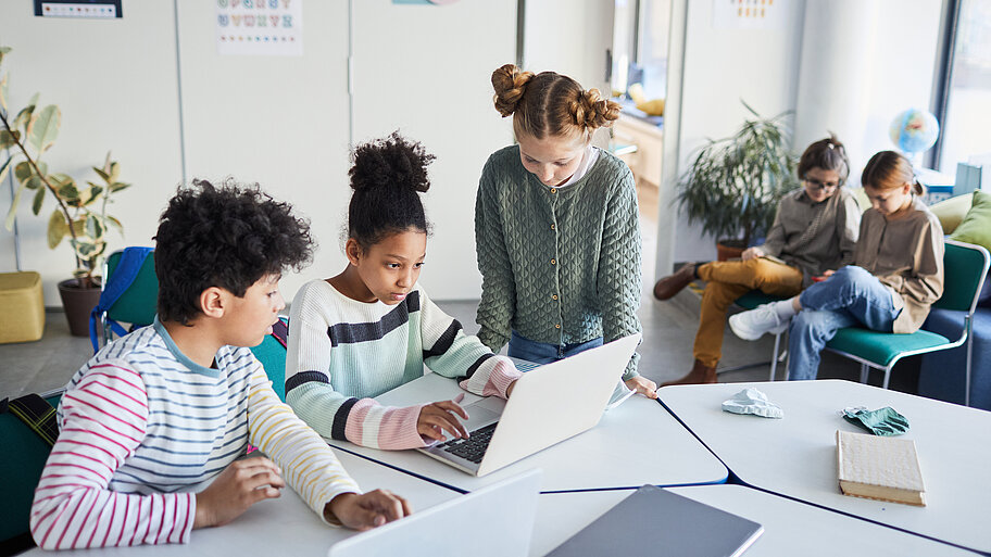 Schülerinnen und Schüler bei Gruppenarbeit mit Laptop. 