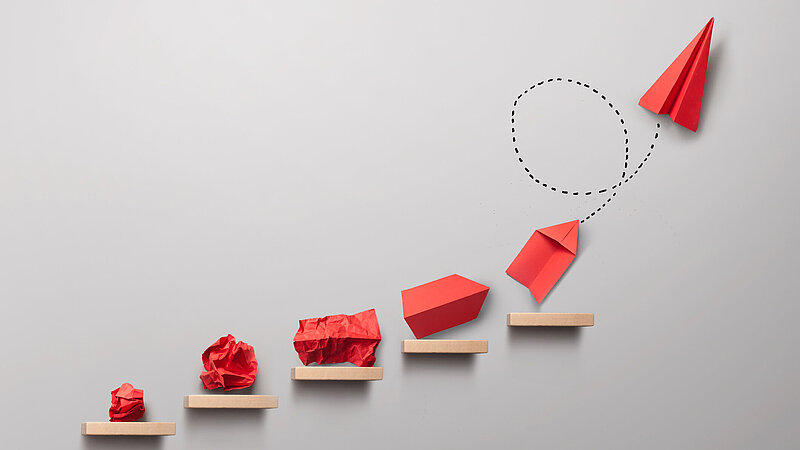 Schrittweise Entstehung eines roten Papierfliegers als Symbolbild für ein Erfolgskonzept