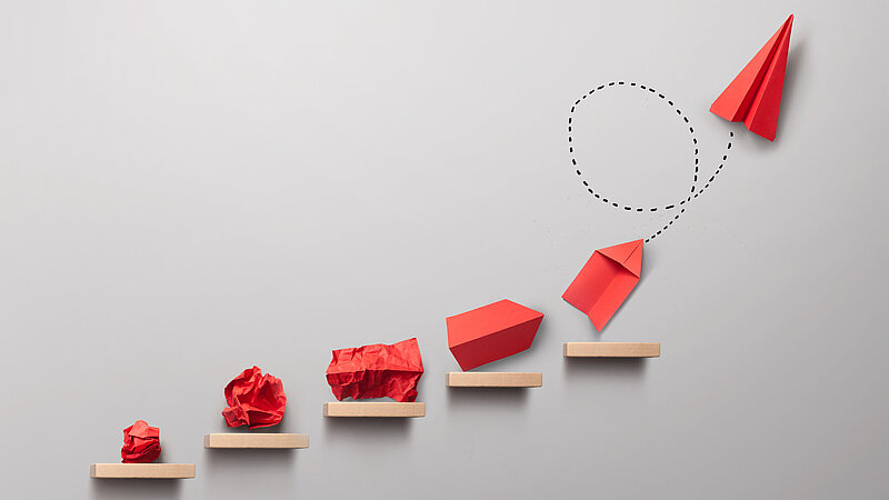 Schrittweise Entstehung eines roten Papierfliegers als Symbolbild für ein Erfolgskonzept