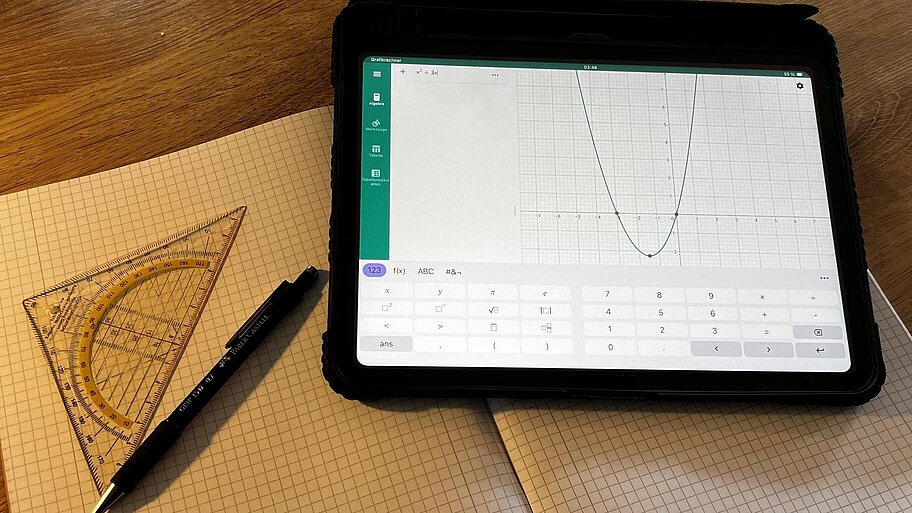 Ein Tablet mit geöffneter Taschenrechner-Anwendung liegt auf einem karierten Papier mit Geodreick und Stift.