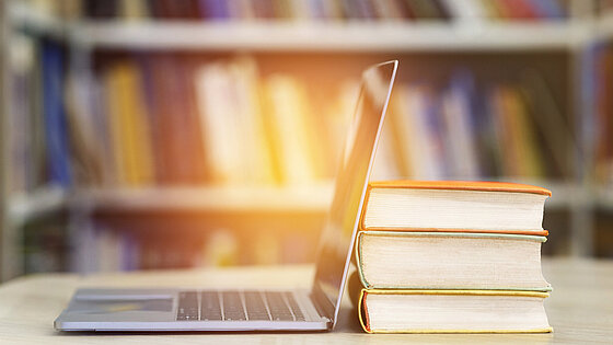 Geöffnetes Laptop neben einem Stapel Bücher
