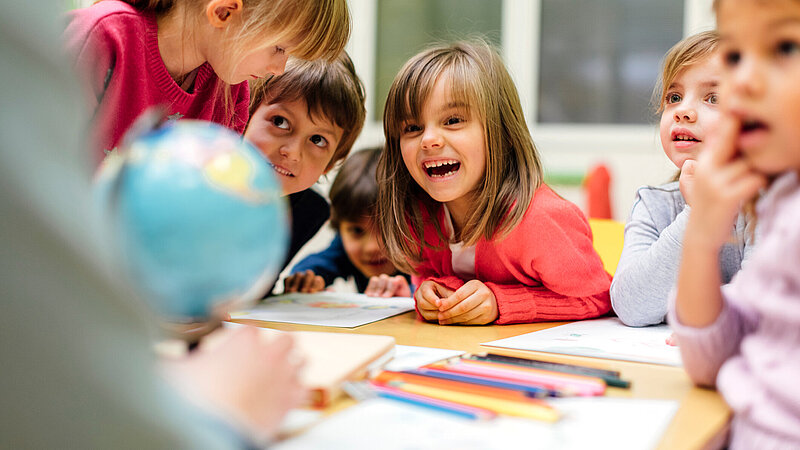 Vorschulkinder und Lehrer sitzen gemeinsam vor einem Globus