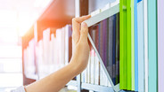 Nahaufnahme: Hand zieht ein e-book aus dem Bücherregal