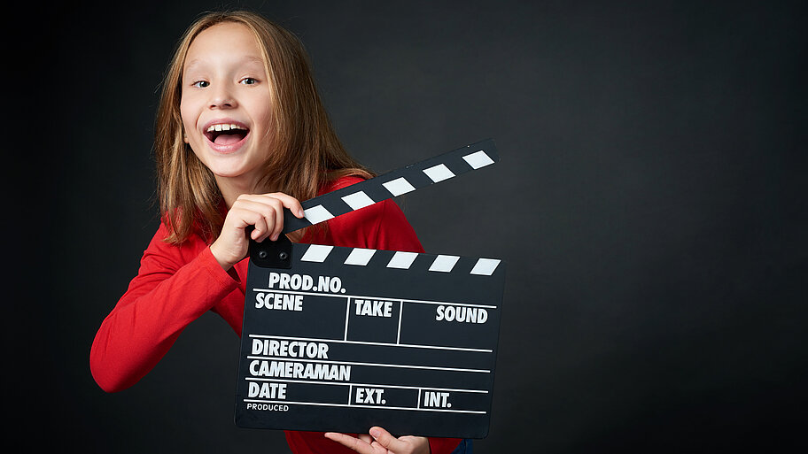 Mädchen hält lachend eine Filmklappe