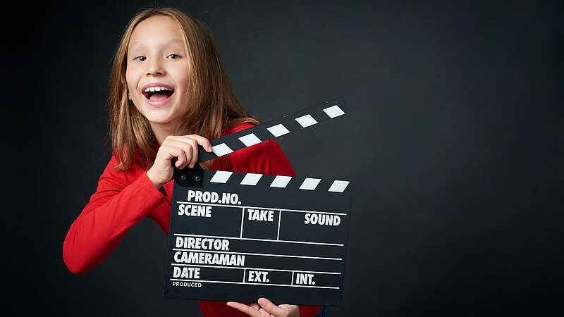 Mädchen hält lachend eine Filmklappe