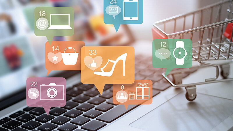 Symbolbild "Online-Shopping": Laptop und Einkaufswagen mit Symbolen von Waren, die online gekauft werden können
