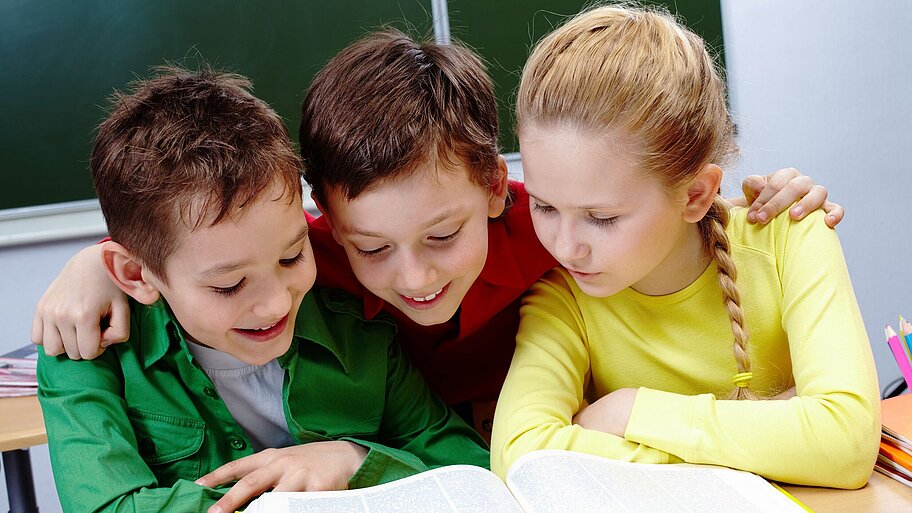 Drei Schüler im Klassenzimmer lesend in einem Buch hinter einer Schulbank