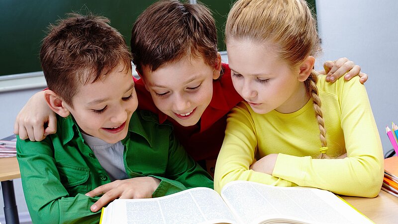 Drei Schüler im Klassenzimmer lesend in einem Buch hinter einer Schulbank