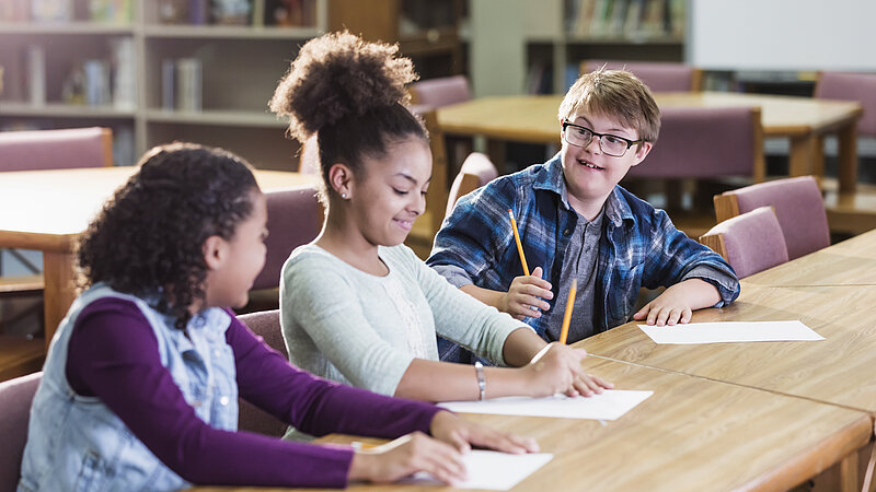 Junge mit Down-Syndrom zusammen mit zwei Mädchen im Klassenzimmer. 