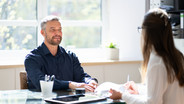 Mann und Frau sitzen sich an einem Besprechungstisch gegenüber zum Vorstellungsgespräch
