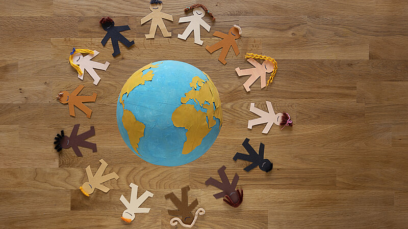 Symbolbild: Multiethnische Papierpuppen mit verschiedenfarbigen Haaren umkreisen eine Weltkugel