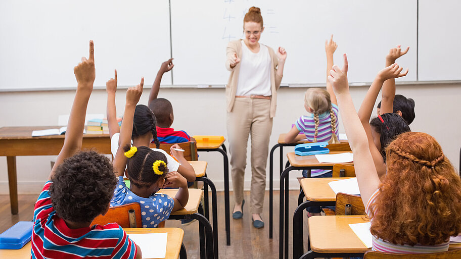 Lehrerin im Klassenzimmer mit Schülern, die sich melden. 