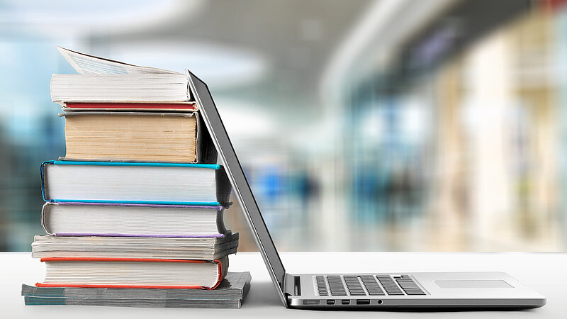 Aufgeklappter Laptop, angelehnt an einen Bücherstapel
