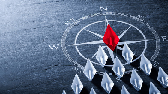 Rotes Papierschiff führt eine Flotte von weißen Papierschiffen über einen Kompass an