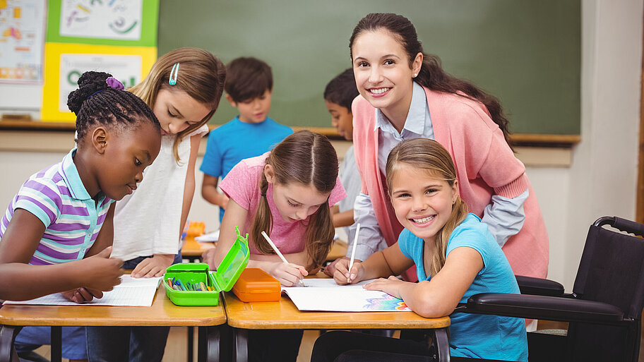 Mehrere junge Schülerinnen mit Lehrerin an Gruppenarbeitstisch