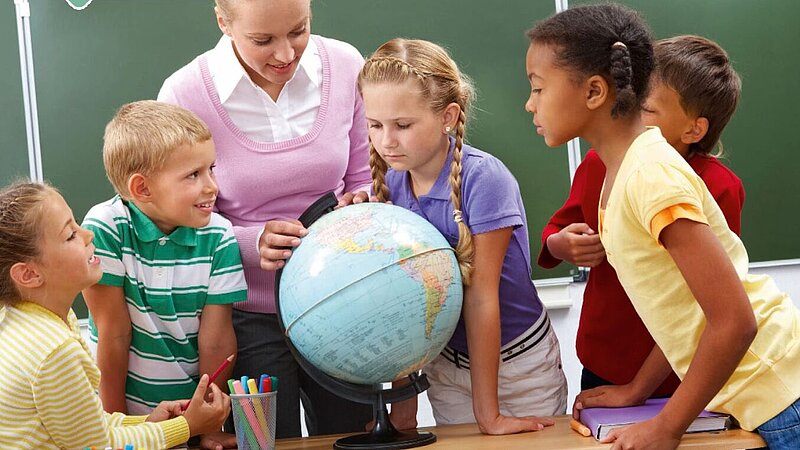 Junge Schülerinnen und Schüler betrachten mit Lehrerin einen Globus. 
